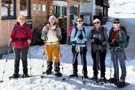 A group of women snowshoers standing in snow in front of a mountain hut