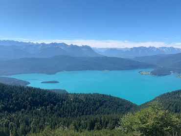 Panoramic view from Jochberg summit over Lake Walchensee in the Bavarian Alps with turquoise water, forested slopes and distant mountain peaks – captured during a guided hike.