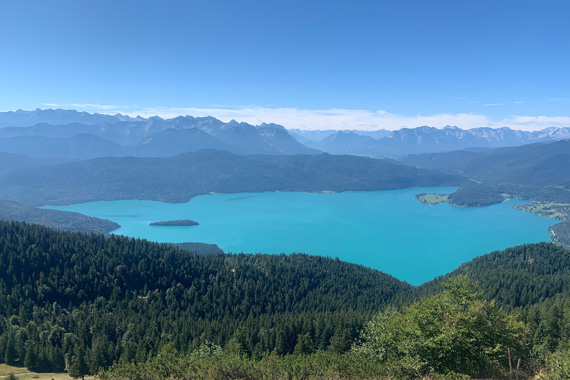 Panoramic view from Jochberg summit over Lake Walchensee in the Bavarian Alps, with turquoise water, forested slopes and distant mountain peaks – typical scenery of the Four Elements guided hikes.