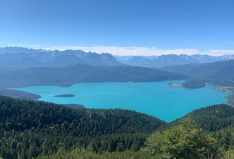Panoramic view from Jochberg summit over Lake Walchensee in the Bavarian Alps, with turquoise water, forested slopes and distant mountain peaks – typical scenery of the Four Elements guided hikes.