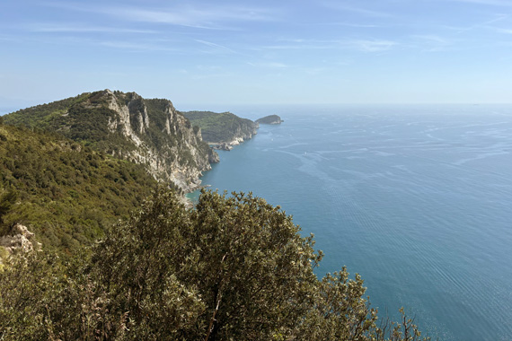 Panoramic view of the Ligurian coastline between Riomaggiore and Portovenere with green hills, cliffs, and blue sea under a clear sky
