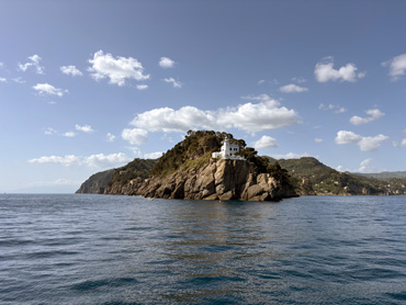 Rocky coastal headland with green hills in the background and calm blue sea under a clear sky