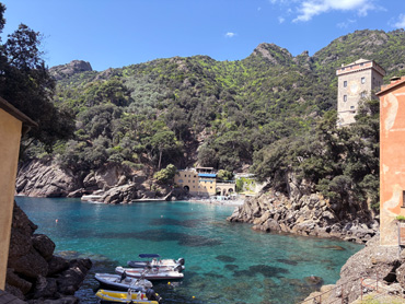 Small boats floating in the turquoise bay of San Fruttuoso surrounded by green hills and historic buildings