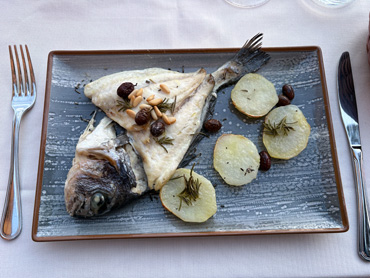Grilled fish served with potato slices and mushrooms on a rectangular plate at an outdoor restaurant in Liguria, Italy