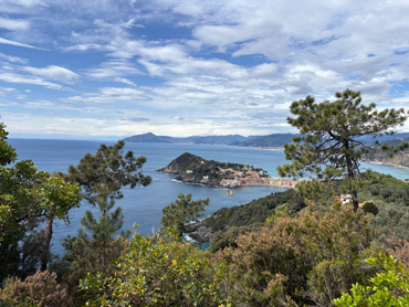 Panoramic view of Portofino peninsula surrounded by blue sea and green hills under a partly cloudy sky