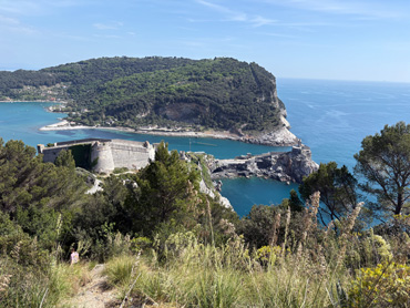 View of Portovenere fortress on a rocky cliff surrounded by green hills and turquoise sea in Liguria, Italy