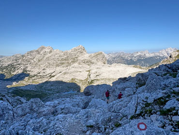 Hikers descending through rugged limestone terrain in Slovenia's Julian Alps with panoramic mountain views