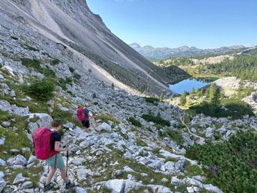 Hikers descending a rocky mountain slope above an alpine lake in Slovenia's Julian Alps