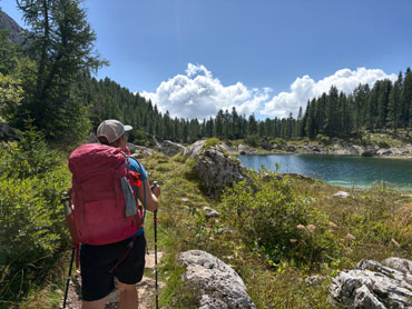 Hiker with a backpack overlooking an alpine lake surrounded by forest and rocky mountain terrain in Slovenia's Julian Alps