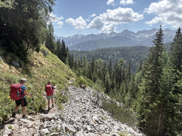 Hiker with a backpack overlooking an alpine lake surrounded by forest and rocky mountain terrain in Slovenia's Julian Alps