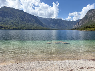 Crystal-clear alpine lake surrounded by forested mountains and rocky peaks in Slovenia's Julian Alps