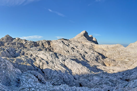 Rugged limestone landscape with jagged alpine peaks under a clear blue sky in Slovenia's Julian Alps