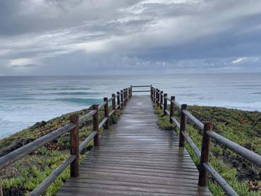 A wooden walkway out to the ocean, with ocean and stormy sky in the background