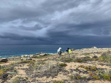 Two walkers on sandy ground watching storm clouds coming over the ocean