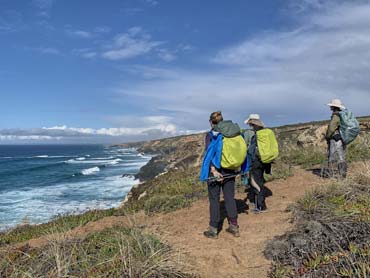 Three hikers captivated by views acrosss the ocean with cliffs and ocean in the backkground