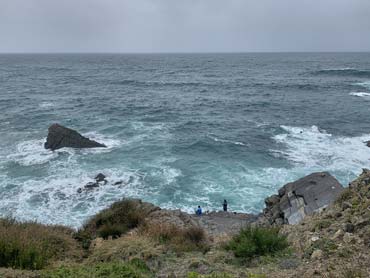 Two fishermen fishing from clifftops with rocks and ocean