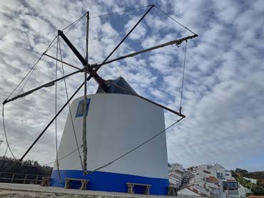 A traditional windmill without sails on a hill with houses in the background